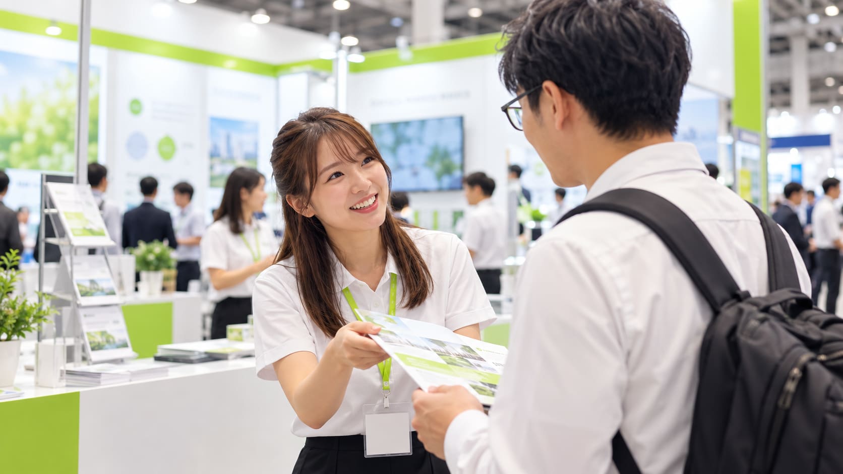 展示会のブースで来場者に資料を渡しながら話しかけるスタッフ